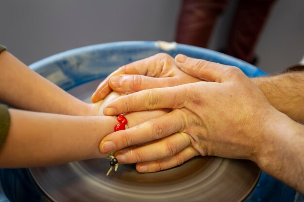 Closeup of a potter's hands and a child's hand with an item on a potter's wheel