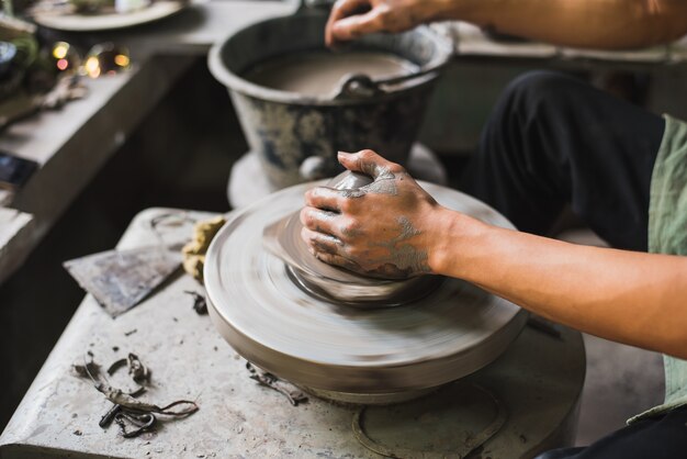 closeup potter's hands shaping soft clay to make an earthen pot