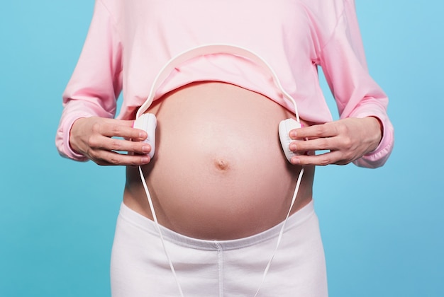 Closeup a pregnant white girl holds white headphones on his belly toddler listens to music