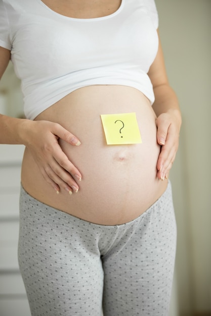 Closeup pregnant with question mark drawn on post-it sticker on belly