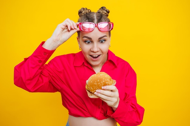 Closeup of a pregnant woman in a bright pink shirt and junk food Hamburger and pregnancy The concept of a pregnant woman eating unhealthy food Cheerful pregnant woman eats fast food