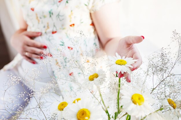 Closeup of pregnant woman holding flower and touching her belly