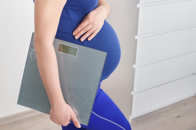 closeup pregnant woman holding scales Pregnancy healthcare control weight gain concept