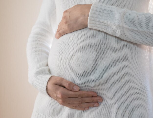 Primo piano di una donna incinta in un maglione bianco che accarezza la sua pancia incinta