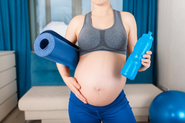 closeup pregnant woman with yoga mat and bottle of water at home Expectant mother after gymnastics Pregnancy gymnastics for pregnant healthy lifestyle concept