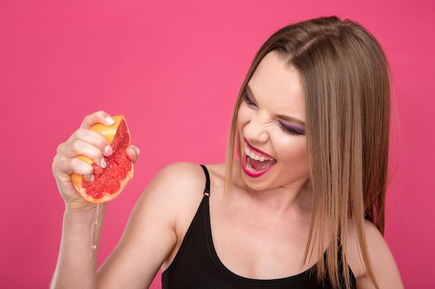 Closeup of pretty excited delighted woman squeezing grapefruit juice by hands