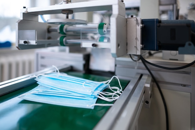 Foto processo di primo piano di maschere mediche realizzate in fabbrica. macchinari automatizzati che producono maschere mediche respiratorie in grandi quantità.