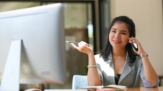 Closeup Professional asian female boss talking on the phone while looking some details at pc screen