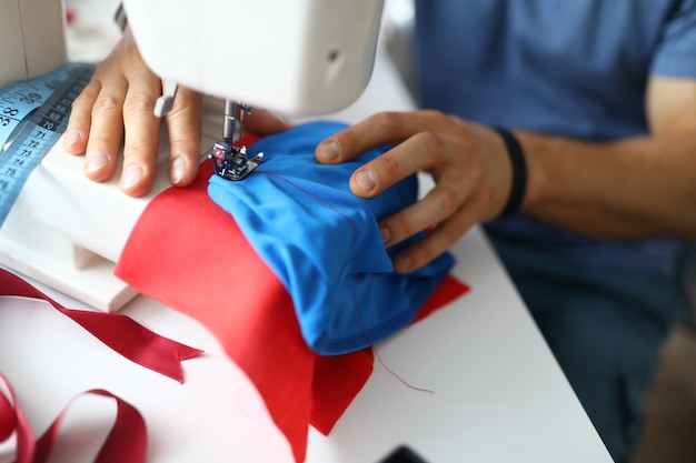 Closeup of professional atelier worker using sewing machine man in protective uniform talented