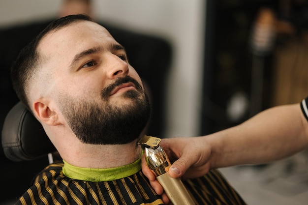 Крупный план профессионального парикмахера подстригает клиенту его бороду красивый бородатый мужчина в парикмахерской