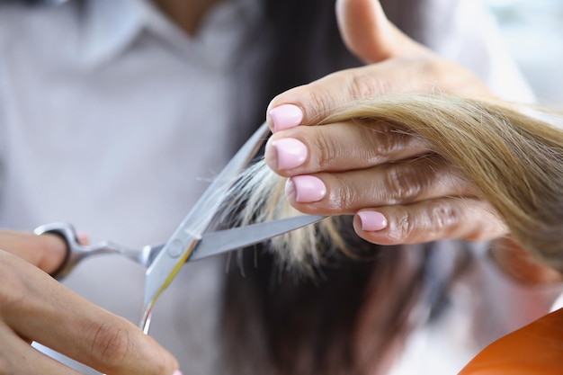 Closeup of professional hairdresser master cutting strand of blonde hair using special