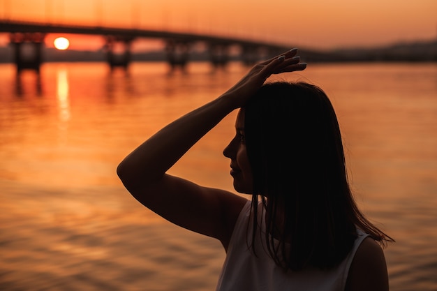 Closeup profiel silhouet van een meisje met een hand op haar hoofd poseren in de buurt van de zee en een brug op een r...