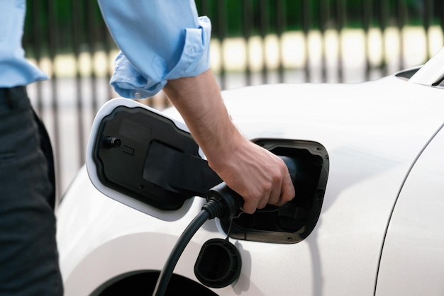 Closeup progressive businessman plugs charger plug from charging station to EV