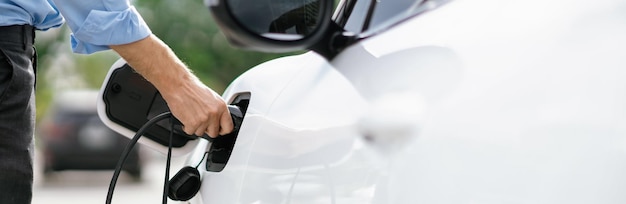 クローズ アップの進歩的なビジネスマンは、充電ステーションから EV に充電器のプラグを差し込みます