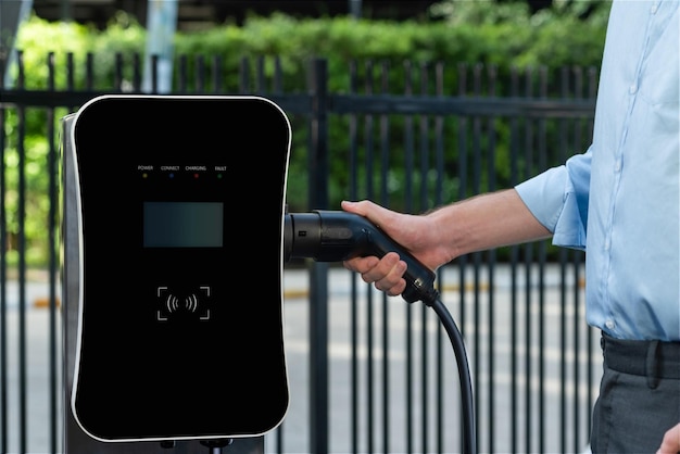 Closeup progressive businessman plugs charger plug from charging station to EV