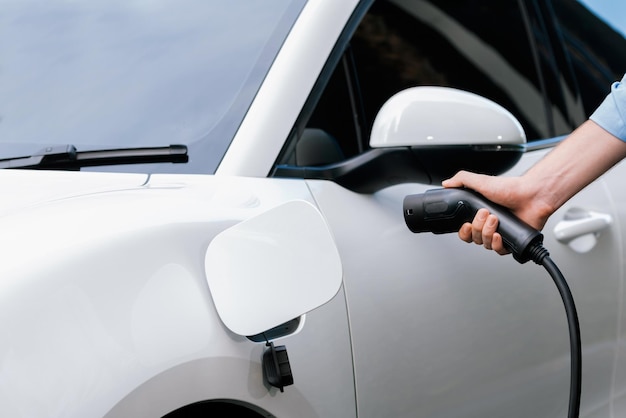 Closeup progressive businessman plugs charger plug from charging station to EV