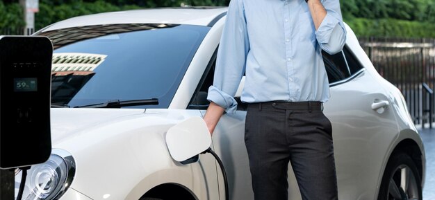 Closeup progressive businessman with electric vehicle at charging station