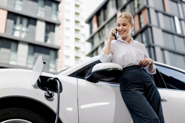 Крупным планом прогрессивная женщина разговаривает по телефону, опираясь на электромобиль
