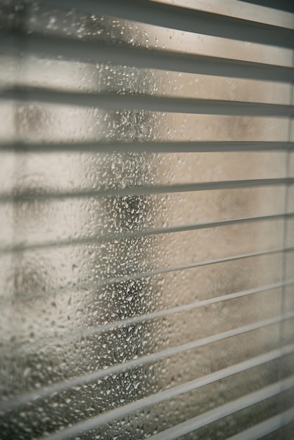 Closeup of rainy water droplets and glass windows with blinds\
macro shot of raindrops on a glass window blinds with water\
drops