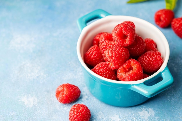Closeup raspberry fruits in blue bowl blue background
