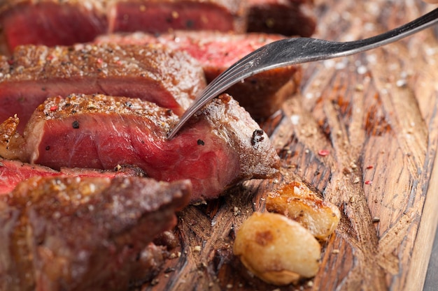 Photo closeup ready to eat steak new york beef breeds of black angus with herbs garlic and butter on a wooden board the finished dish for dinner the finished piece of steak skewered on a fork