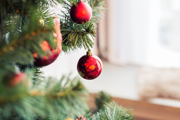 Крупный план красных безделушек вися от украшенной рождественской елки.