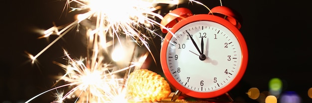 Closeup of red clock showing five before midnight