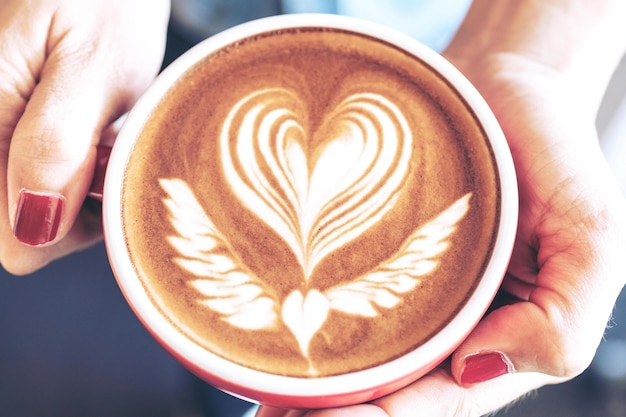 Closeup of a red cup of coffee latte art on woman hand in coffee shop cafe