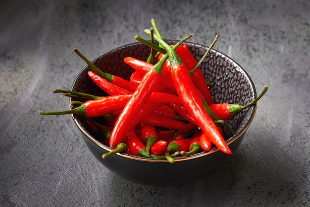 Closeup on red hot chili peppers in black ceramic bowl over dark textured table