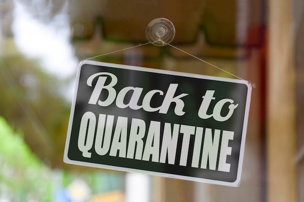 Closeup on a red open sign in the window of a shop displaying the message Back to quarantine