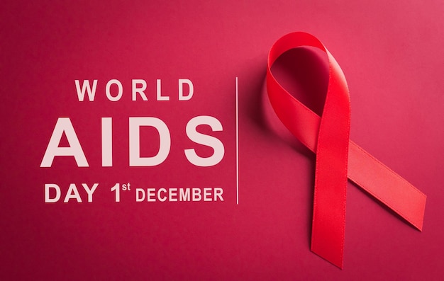 Closeup red ribbon HIV world AIDS day awareness ribbon and the text on red background Healthcare and medicine concept