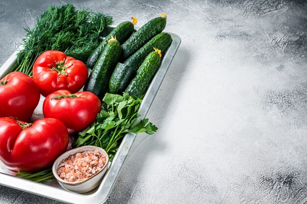 Closeup of red tomatoes and green cucumbers with herbs in a kitchen tray. White background. Top view. Copy space.