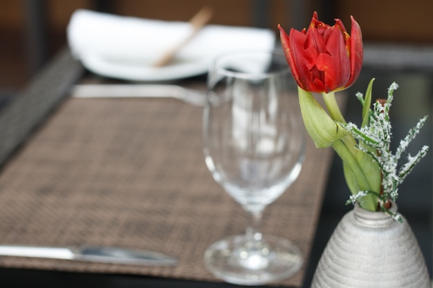 Closeup of a red tulip in a small vase over the table with a wine glass in a cafe or restaurant