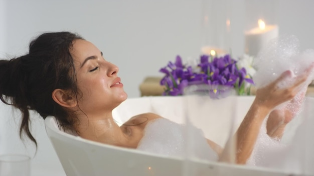 Closeup relaxed woman blowing foam at bath Smiling woman having fun with foam