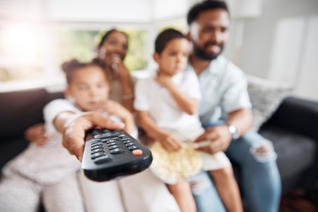 Closeup of remote control with family watching tv in their living room together Parents and kids relaxing on the sofa enjoying a movie series or cartoons in the lounge at home while bonding