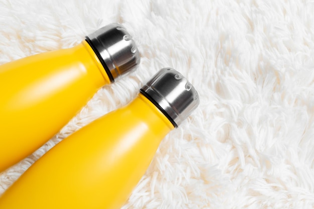 Closeup of reusable eco water bottles of yellow color on white fluffy plaid