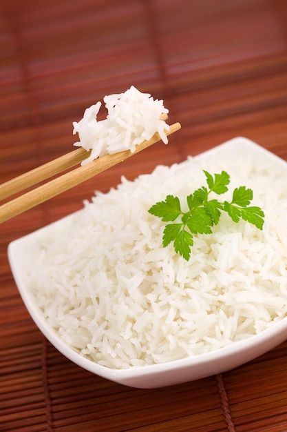 Closeup of rice on chopsticks and a bowl on mat