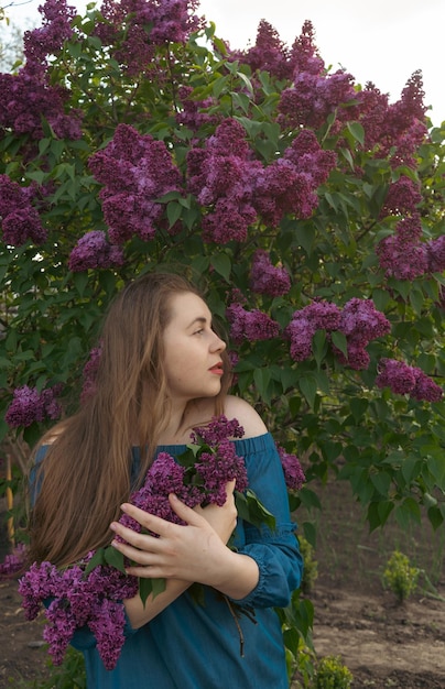 Closeup romantic young woman portrait in blooming lilac garden Spring story The brownhaired woman smiles with a flower in her hair closing her eyes and enjoying the spring mood