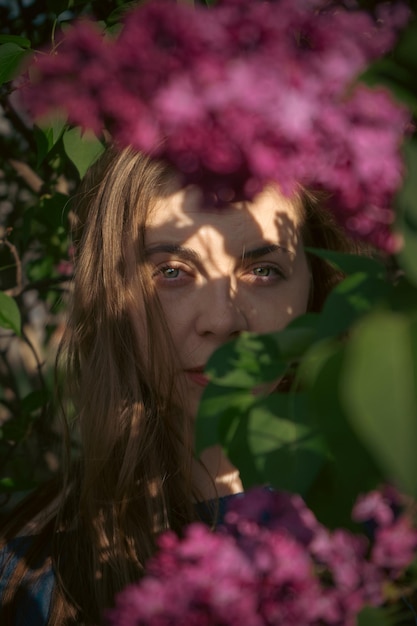 Closeup romantic young woman portrait in blooming lilac garden Spring story The brownhaired woman smiles with a flower in her hair closing her eyes and enjoying the spring mood