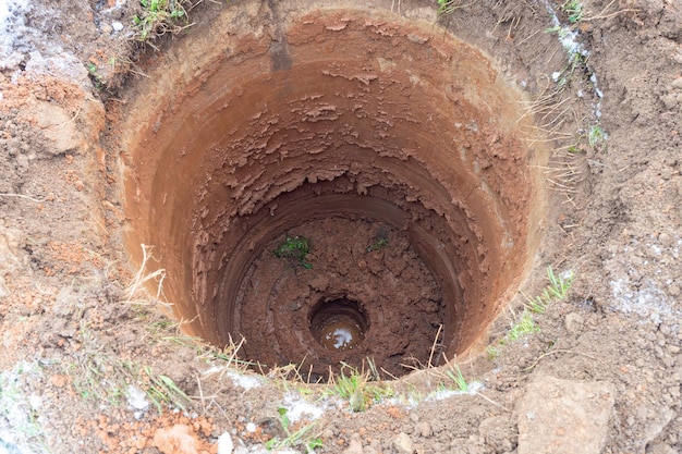 Primo piano di un buco rotondo nel terreno scavare un pozzo d'acqua sotto l'approvvigionamento idrico di terra di fango