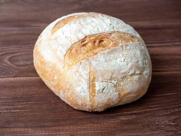 Closeup of a round loaf of wheat bread lying on a brown wooden background Baking bakery concept Side view