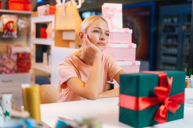 Closeup of sad attractive young sales woman sits at counter of holiday store in mall waiting for cus...