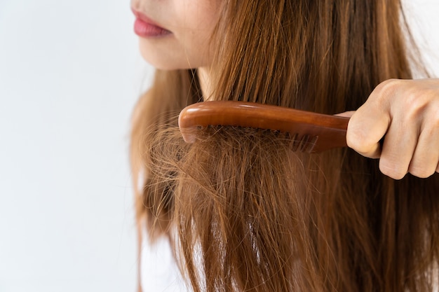 Closeup of sad young Asian girl brush her damaged hair. Isolated on white background with copy space