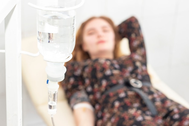 Photo closeup of saline drip with background woman patient on the bed