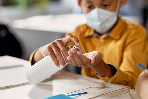 Closeup of schoolboy disinfecting his hands in the classroom