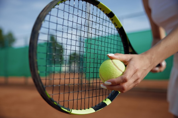 Closeup selective focus on ball and tennis racket in female hand. Private training sports club and professional equipment for game concept