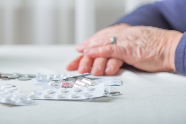 Closeup senior woman hands with pills and coins on table at
home. an elderly pensioner counts money.