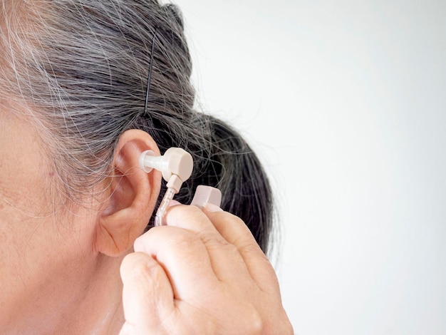 Closeup of a senior woman inserting a hearing aid in her ear