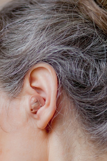 Closeup senior woman inserting hearing aid in her ears