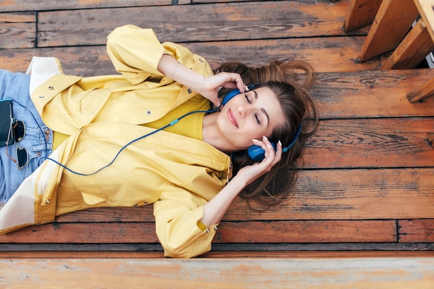 Photo closeup sensual portrait of young smiling happy woman posing with blue earphones outdoor